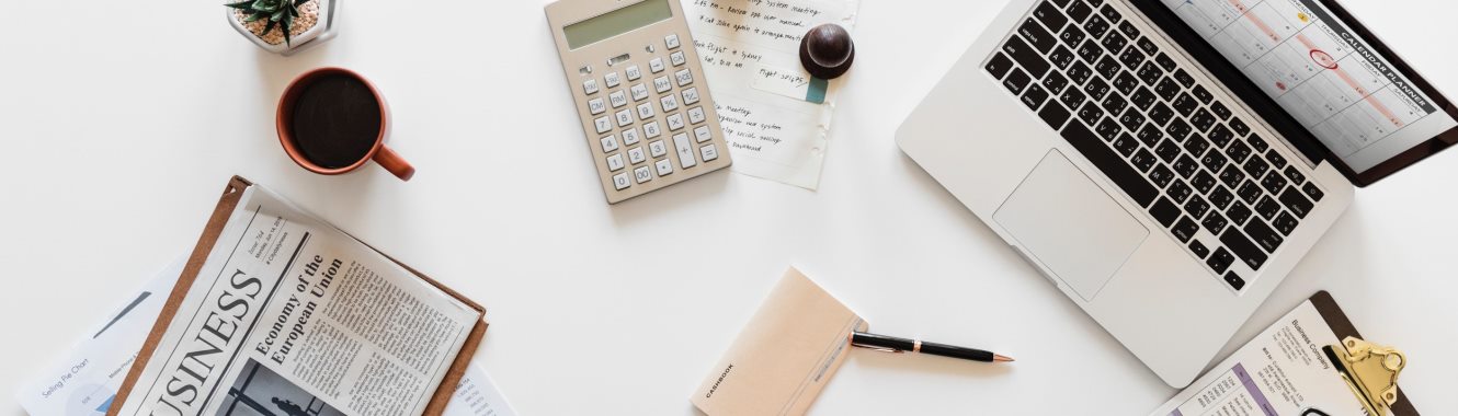 Work desk with laptop, news paper, calculator and checkbook.