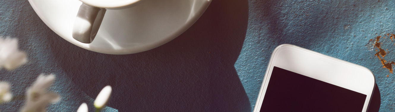 A mobile phone on a table next to coffee cup