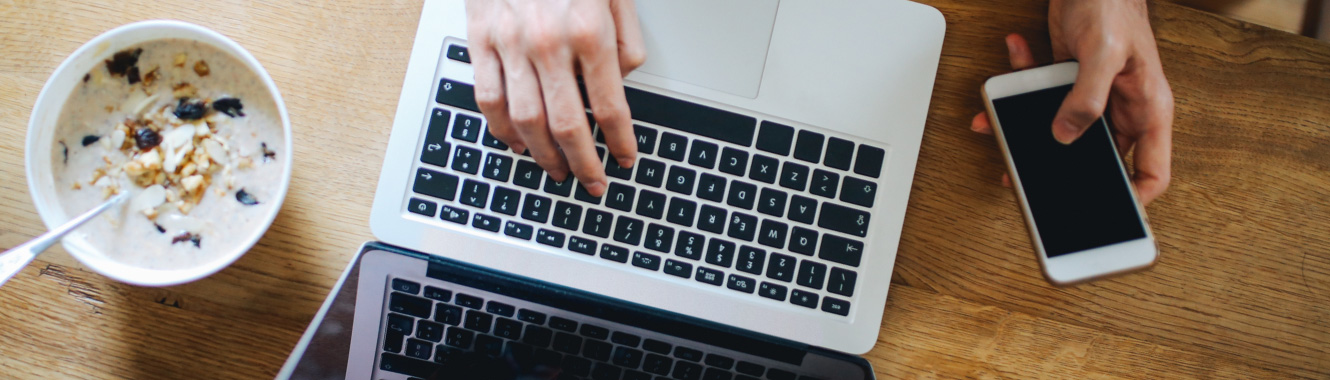 A person eating breakfast next to laptop