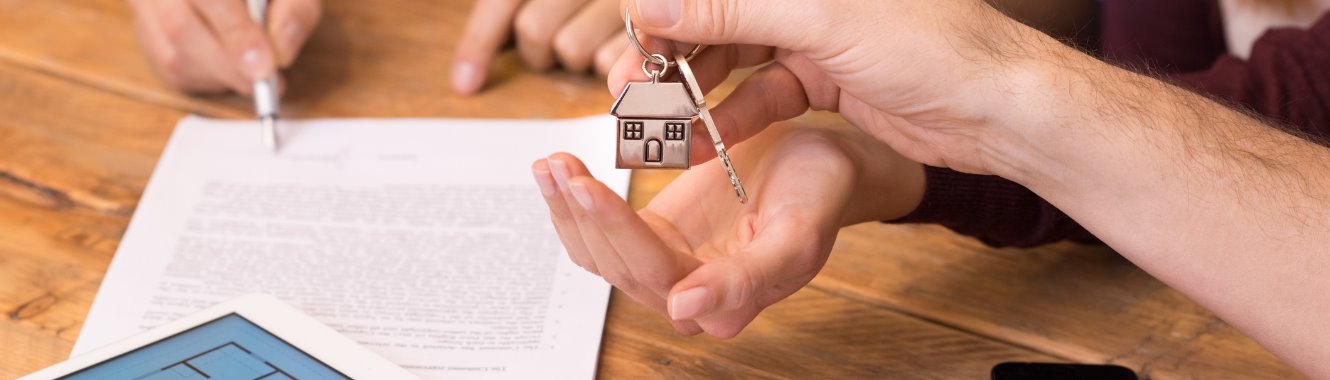 person signing a document while being handed a set of keys with a house keychain attached