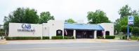 Long white building with blue metal roof and large windows.