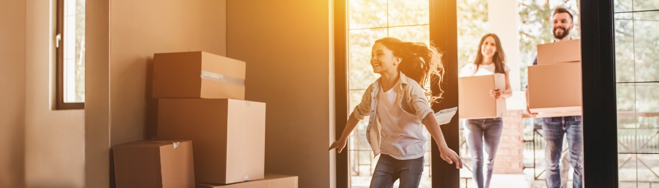 Girl running through new home with parents carrying in boxes as family moves in